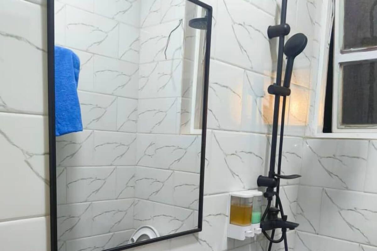 Un baño con baldosas de mármol blanco, un lavamanos blanco, un espejo y un cabezal de ducha de mano.