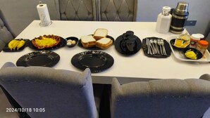 Una mesa de comedor con diferentes alimentos y utensilios, en una habitación con sillas tapizadas en gris.