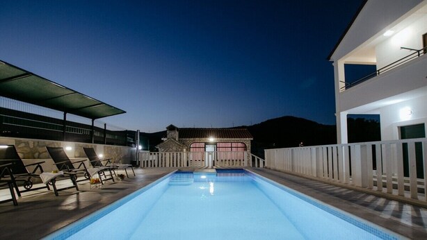 A rectangular swimming pool with a white fence and lounge chairs on one side, and a building with a balcony on the other.