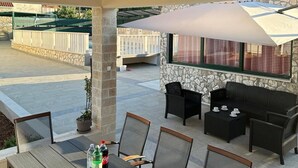 An outdoor patio with a wooden ceiling, stone walls, and a seating area with a table and chairs.
