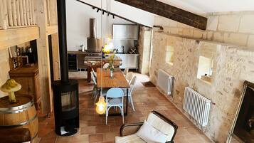 Un intérieur rustique avec une table à manger en bois, des chaises, un canapé, une cheminée et un coin cuisine.