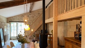 A rustic dining area with a wooden table and chairs, a vase with flowers, and a staircase leading to an upper level. - La CLOCHETTE / La MAISONNETTE, La MAISONNETTE (Lugon-et-l'Île-du-Carnay)