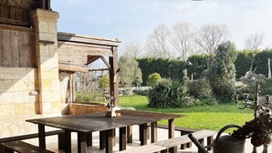 An outdoor patio with wooden tables and benches, a stone wall, and a garden with trees and shrubs. - La CLOCHETTE / La MAISONNETTE, La MAISONNETTE (Lugon-et-l'Île-du-Carnay)