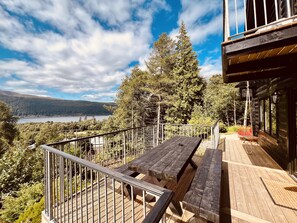 A wooden deck with picnic tables overlooking a lake and forested hills.