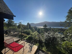A wooden deck with a red chair, overlooking a mountainous landscape and a body of water.