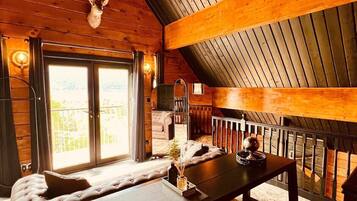 Een gezellig chaletinterieur met een houten plafond, een open haard, een bank en een eettafel.