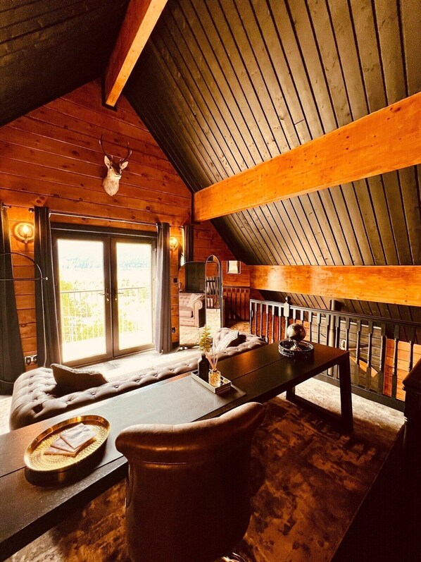 A cozy cabin interior with a wooden ceiling, a fireplace, a sofa, and a dining table.