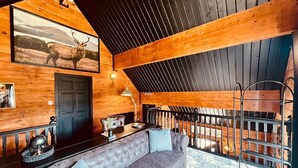 A cozy log cabin interior with a gray tufted sofa, a wooden ceiling, and a framed deer picture on the wall.