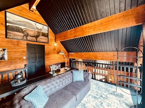 L’intérieur d’un chalet confortable, avec un canapé gris à motifs capitonnés, un plafond en bois et un tableau représentant un cerf, encadré et accroché au mur.