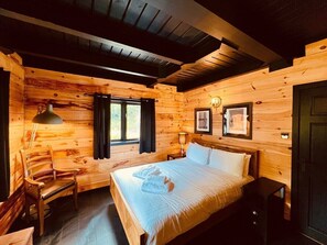 Una habitación de cabaña de madera con una cama, una silla, un escritorio y una ventana.