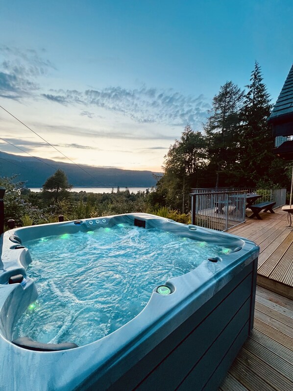 Un bain à remous sur une terrasse en bois, avec vue sur les montagnes et les arbres.