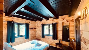 A wooden cabin room with a bed, two windows, a desk, and a chair.