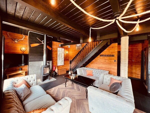 A cozy living room with a fireplace, a staircase, and a modern chandelier.