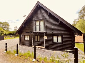 A log cabin with a balcony, a gravel driveway, and a rope barrier.