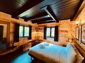 A cozy wooden cabin room with a bed, a chair, a table, and a window.