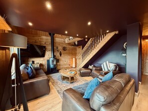 Una sala de estar acogedora con chimenea, sofás de cuero, una mesa de centro y una escalera.