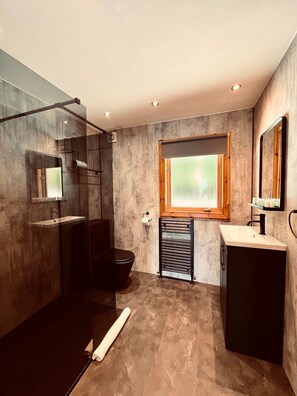 A modern bathroom with a glass shower enclosure, a toilet, a sink with a mirror, and a window providing natural light.