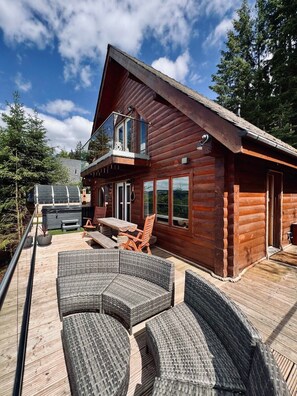 A wooden cabin with a deck, outdoor seating, and a hot tub.