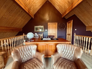 Una habitación con techos altos, un escritorio de madera, dos sillones de cuero, un globo terráqueo y una puerta rústica.