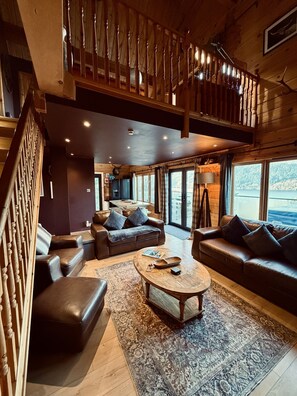 A spacious living area with a high ceiling, wooden staircase, and large windows offering a view of the outdoors. - Luxury lodge on Loch Ness + hot tub & sauna (Inverness)