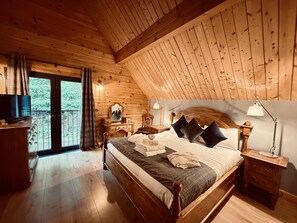 Une chambre dans une cabane en bois, comprenant un lit, des tables de chevet, une commode et un balcon agrémenté de rideaux.