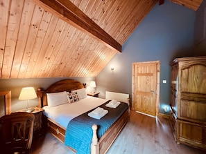 Une chambre confortable avec un plafond en bois, un lit recouvert d’une couverture bleue, deux lampes de chevet et une armoire en bois.