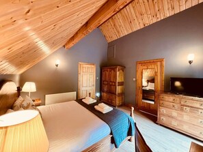 Une chambre avec un plafond en bois, un lit, une commode, un téléviseur et une armoire.