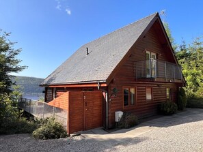 Une cabane en rondins avec un balcon, un garage et une vue sur le lac.