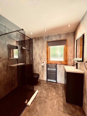 Une salle de bain moderne dotée d’une douche à parois de verre, de toilettes noires, d’un meuble-lavabo avec miroir et d’une fenêtre laissant entrer la lumière naturelle.