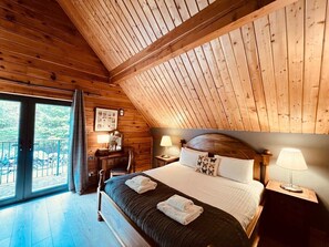 Une chambre dans une cabane en bois, avec un grand lit, deux tables de chevet avec des lampes, un bureau et une chaise.
