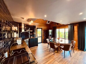 A modern kitchen with a central island, wooden flooring, and a dining area with a round table and chairs. - Luxury Loch Ness lodge with hot tub & sauna (Inverness)