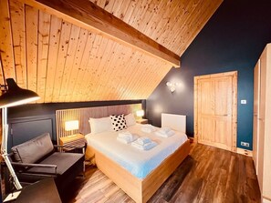 A bedroom with a wooden ceiling, a bed with white linens, a nightstand, a chair, and a wall-mounted lamp. - Luxury Loch Ness lodge with hot tub & sauna (Inverness)