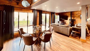 Una sala de estar moderna con techo de madera, un comedor con mesa de vidrio y una cocina con estufa.