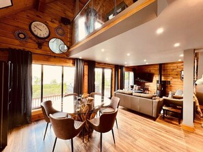 Un salon moderne avec un plafond en bois, un coin repas doté d’une table en verre et une cuisine équipée d’une cuisinière.