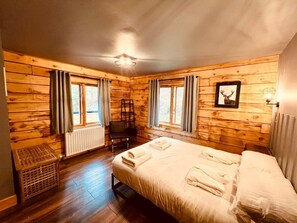 Una habitación con paneles de madera, una cama, dos ventanas con cortinas, un radiador y un cuadro en la pared.