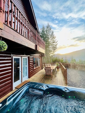 A wooden cabin with a deck, a hot tub, and a scenic mountain view.