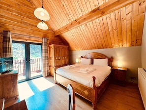 Un dormitorio con paneles de madera, una cama grande, un televisor y un gran ventanal corredizo que da a un área exterior.