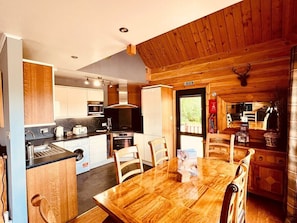 A compact kitchen with a dining area, wooden walls, and a mounted deer head. - Group lodge with hot tub and fire pit (Inverness)