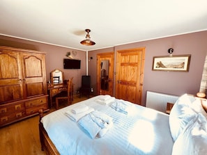 A bedroom with a bed, wooden wardrobe, a desk, and a radiator.