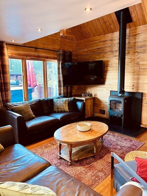 A cozy living room with a sofa, a coffee table, and a TV. There's a wooden ceiling and a fireplace.