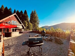 A barbecue area with a grill, a wooden deck, and a view of a mountain range. - Group lodge with hot tub and fire pit (Inverness)