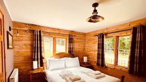 A wooden-paneled bedroom with a large bed, two bedside tables, a ceiling fan, and windows with curtains. - Group lodge with hot tub and fire pit (Inverness)