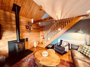 A cozy living room with a wood-burning stove, a staircase, and a sofa.