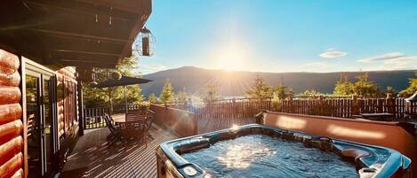 A hot tub on a wooden deck with a view of mountains and a clear sky.