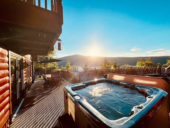 A hot tub on a wooden deck with a view of mountains and a clear sky.