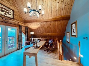 A cozy room with a wooden ceiling, a dining table, a sofa, and a chair. There is a chandelier hanging from the ceiling. - Group lodge with hot tub and fire pit (Inverness)
