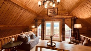 A cozy attic room with a wooden ceiling, a sofa, a table, and a chandelier. - Group lodge with hot tub and fire pit (Inverness)