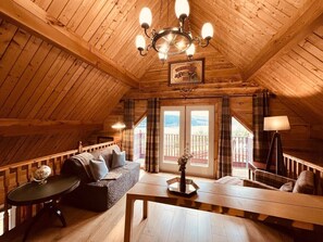 A cozy attic room with a wooden ceiling, a sofa, a table, and a chandelier.