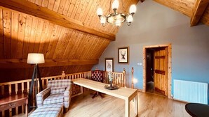A cozy loft-style room with a high ceiling, wooden beams, a long wooden table, a plaid sofa, and a chandelier. - Group lodge with hot tub and fire pit (Inverness)