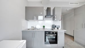 A modern kitchen with grey cabinetry, a built-in oven, and a stainless steel range hood. - Hotel Studio Apartment in East London (Ilford)